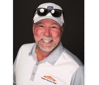 male smiling, wearing servpro logo'd shirt with white baseball cap and sunglasses resting on cap